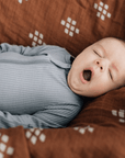 yawning baby laying on cotton muslin quilt, chestnut textiles
