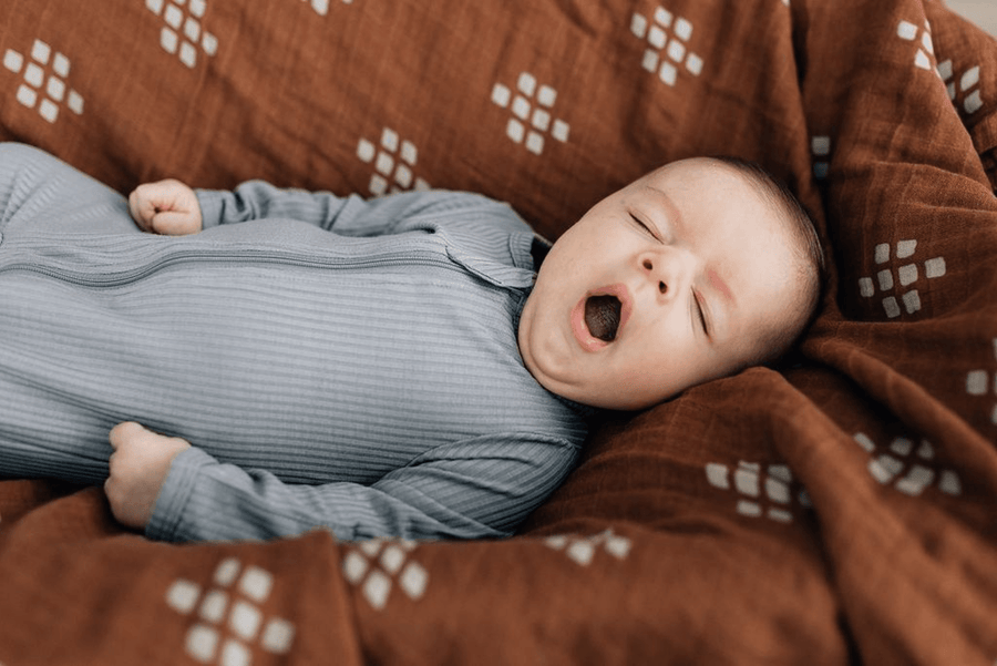 yawning baby laying on cotton muslin quilt, chestnut textiles
