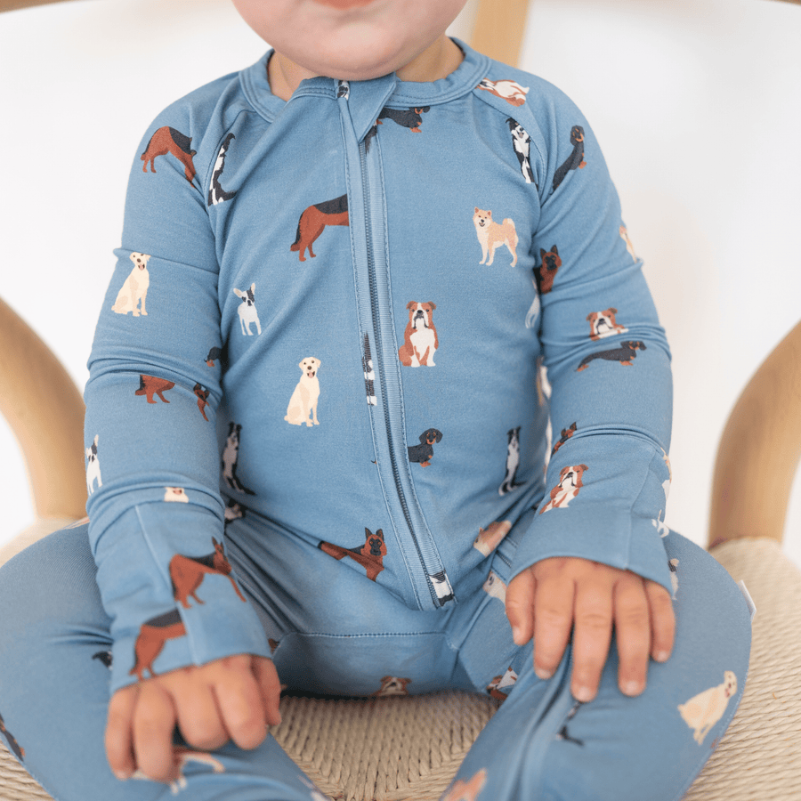 Child wearing a blue onesie with dog pattern sitting on a beige chair.